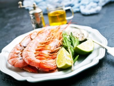 Platter of fresh shrimp with lime, rosemary, and dipping sauce on a plate; seafood cuisine, gourmet meal presentation.
