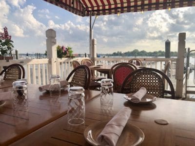 Outdoor dining at sea shore restaurant with ocean view, wooden tables, chairs, and canopy under a cloudy sky.